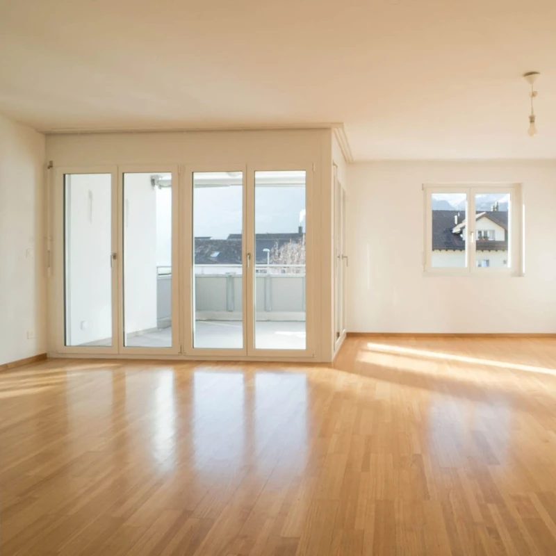 Helles Wohnzimmer mit Parkettboden, großen Fenstern und Zugang zu einem modernen Balkon.